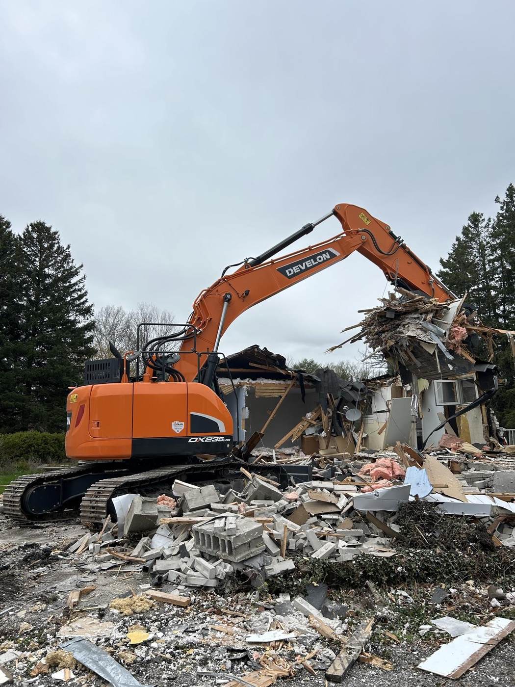 Orange Develon DX235 excavator demolishing a house at a DeEx jobsite